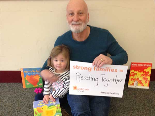 Grandfather sitting on the floor with arm around grandchild, reading together