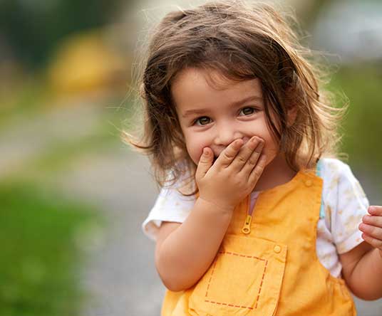 child-outside-hand-over-mouth child giggling with hand over her mouth