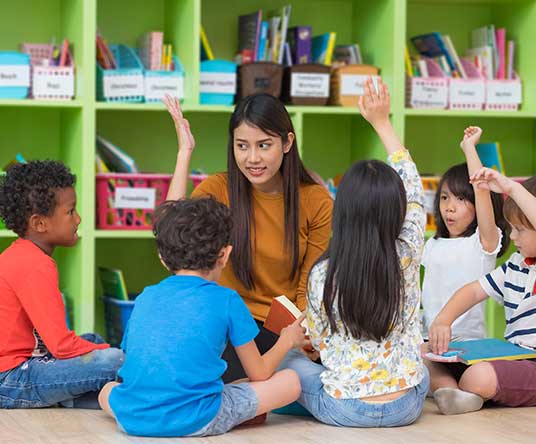 kids and teacher raising their hands while sitting in a reading circle