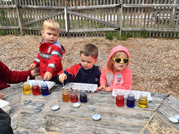 3 kids sitting at a wooden table outside, playing with dyes