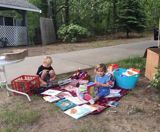kids-playing-by-walkway Kids looking through books while sitting on blanket outside