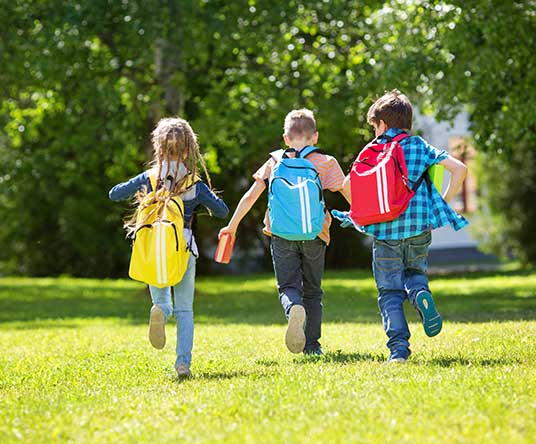 three kids running through yard with backpacks on