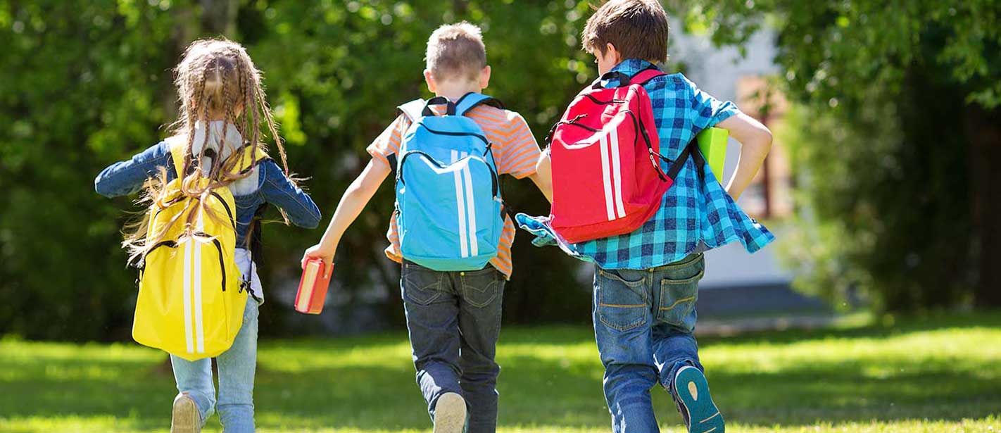 three kids running through yard with backpacks on