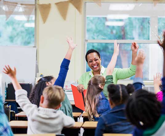 young students raising their hands in a classroom with a teacher